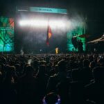 Multitud disfrutando de un concierto nocturno en el Austin City Limits Music Festival, con iluminación dramática y banderas ondeando, reflejando la vibrante atmósfera del evento