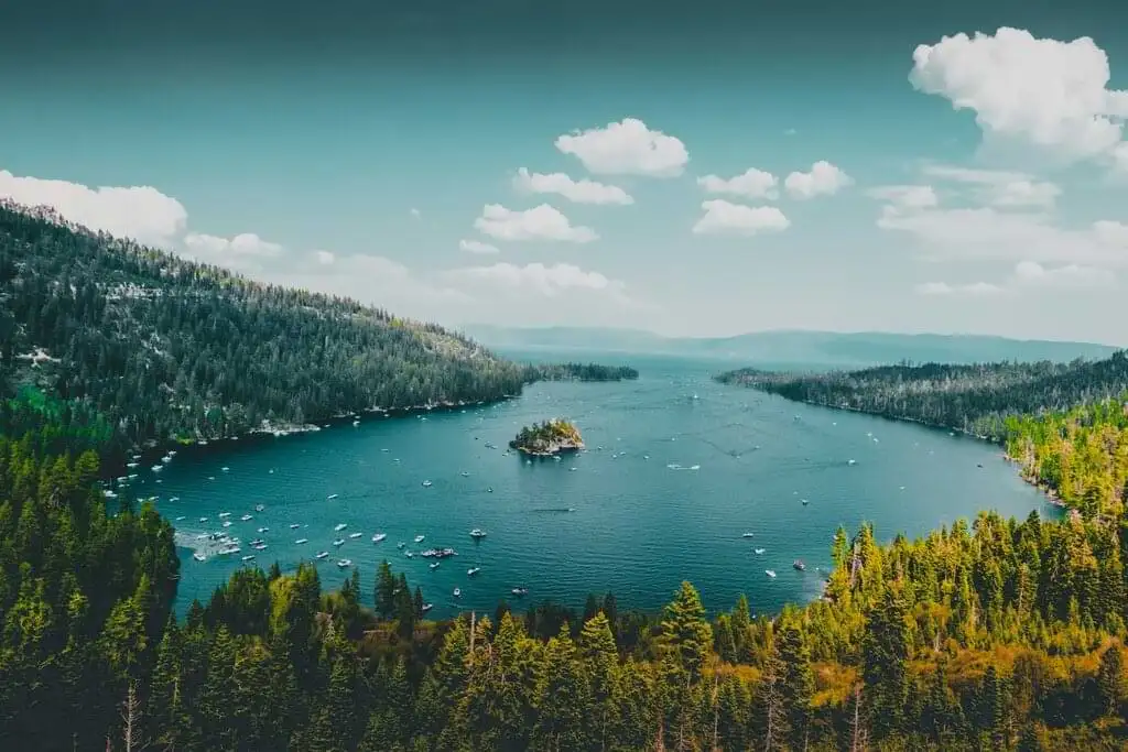 Vista aérea de un lago sereno con una isla pequeña en el centro y montañas boscosas en el fondo