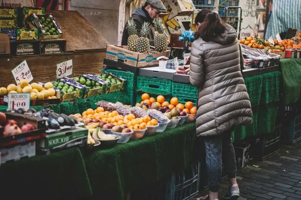 Una persona comprando en un puesto de mercado lleno de frutas frescas como aguacates, limones y naranjas, capturando la esencia de la vida urbana