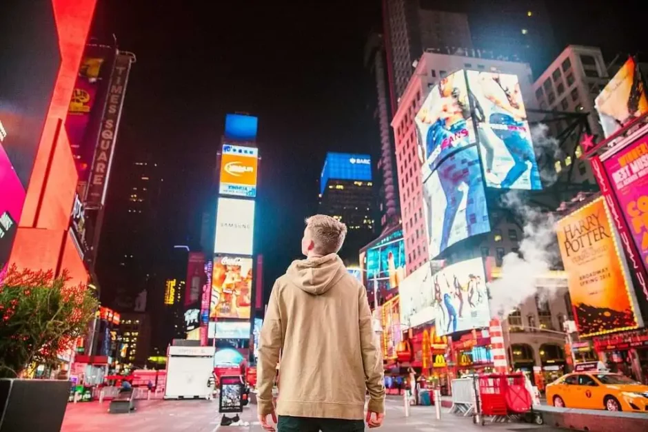 Hombre de espaldas contemplando las vibrantes luces y pantallas publicitarias en Times Square, Nueva York, de noche