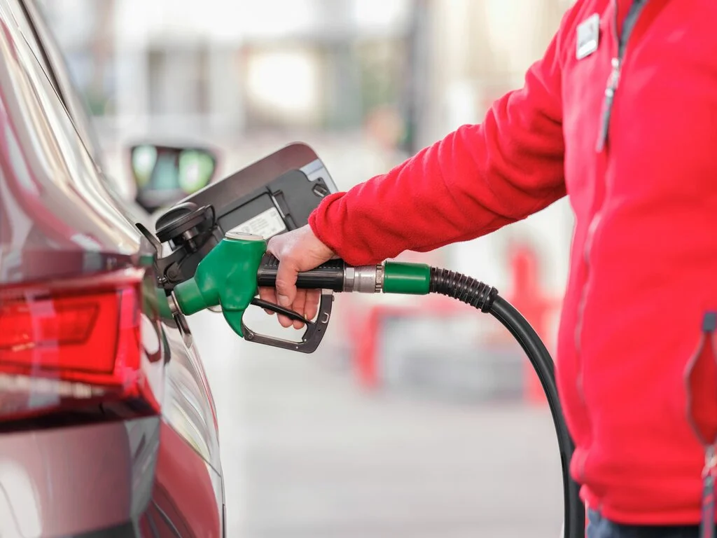 Mano sujetando una manguera de combustible, rellenando el tanque de un coche, en un acto rutinario que conecta con la jornada diaria