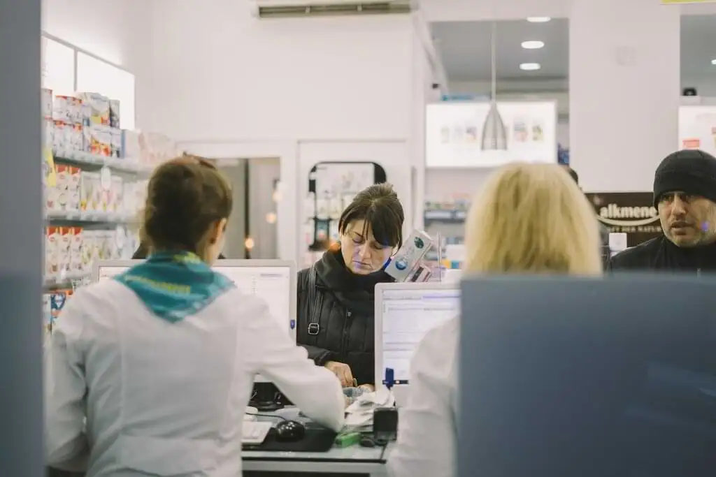 Una farmacéutica atiende a clientes detrás del mostrador en una farmacia moderna y luminosa