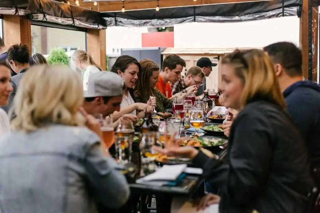 Personas disfrutando de comidas y cervezas en una mesa larga, en un ambiente de cervecería informal y acogedor