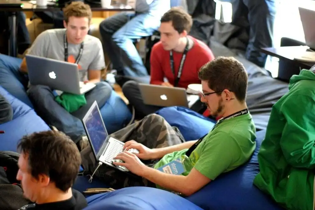 Grupo de programadores enfocados trabajando en sus portátiles en una sala informal con pufs, reflejando un ambiente de coworking tecnológico y colaboración