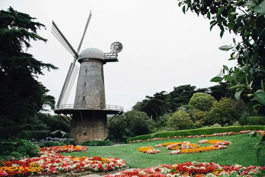 Antiguo molino de viento rodeado de jardines coloridos en un día nublado, un remanso de tranquilidad y belleza natural