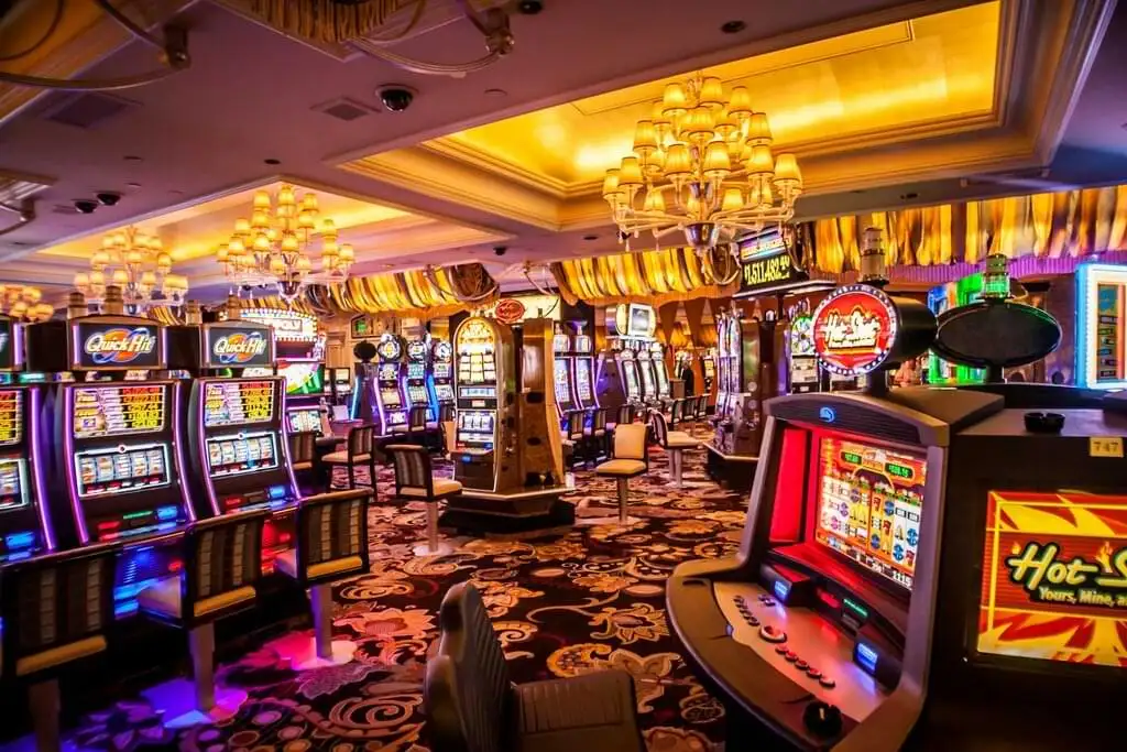 Sala de tragamonedas en un casino de Las Vegas con varias máquinas alineadas y encendidas. La decoración incluye alfombras ornamentadas y candelabros dorados. El ambiente es vibrante y lleno de color, típico de los casinos de la ciudad.