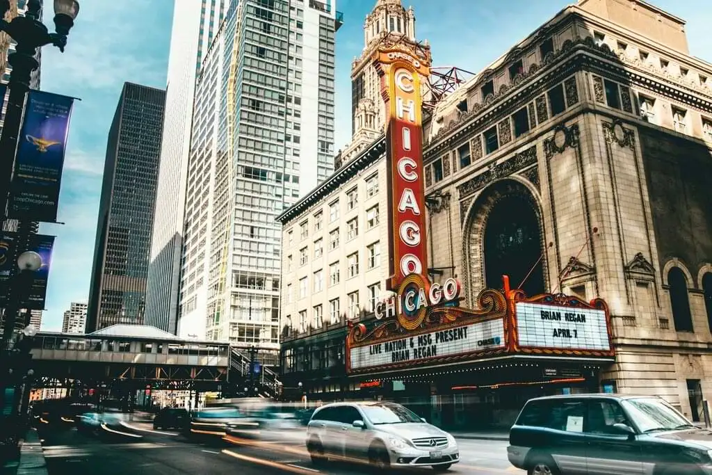 Fachada del histórico Teatro Chicago en el centro de la ciudad, con su distintivo letrero de neón y el bullicio del tráfico urbano en primer plano. Este teatro es un emblema cultural y arquitectónico de Chicago